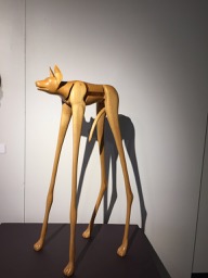 Wooden sculpture of a little dog with very tall skinny legs.