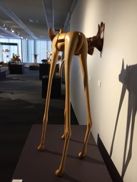 Rear view of a wooden sculpture of a very small dog on very tall skinny legs.