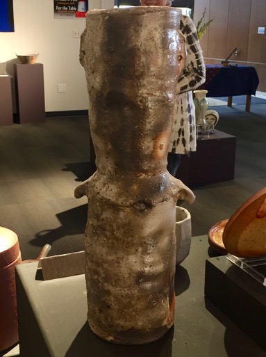Close up color photograph of a tall narrow vase on display in a gallery.